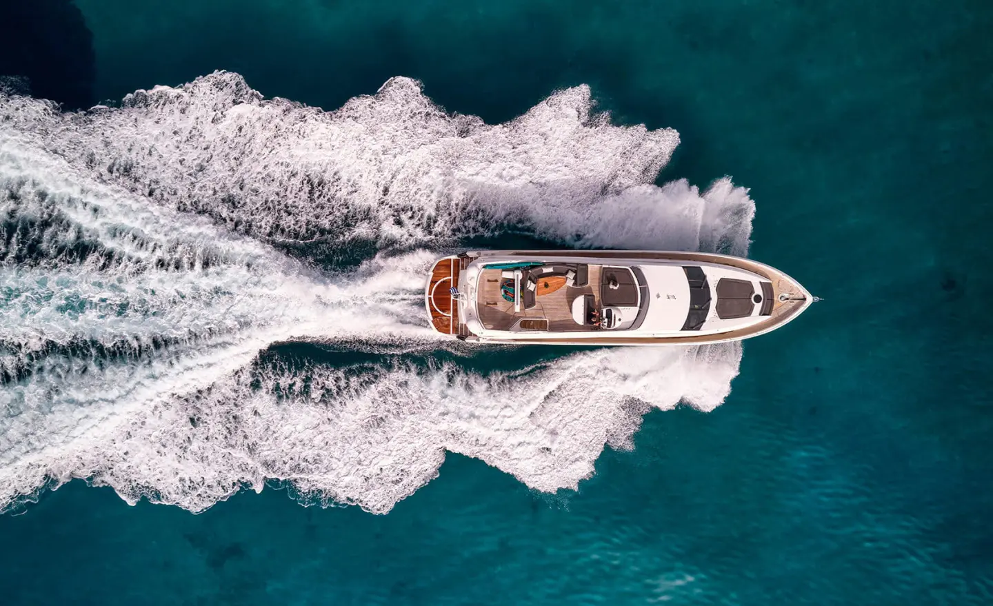 Aerial view of a white motor yacht M Five cruising blue-green sea, wake visible