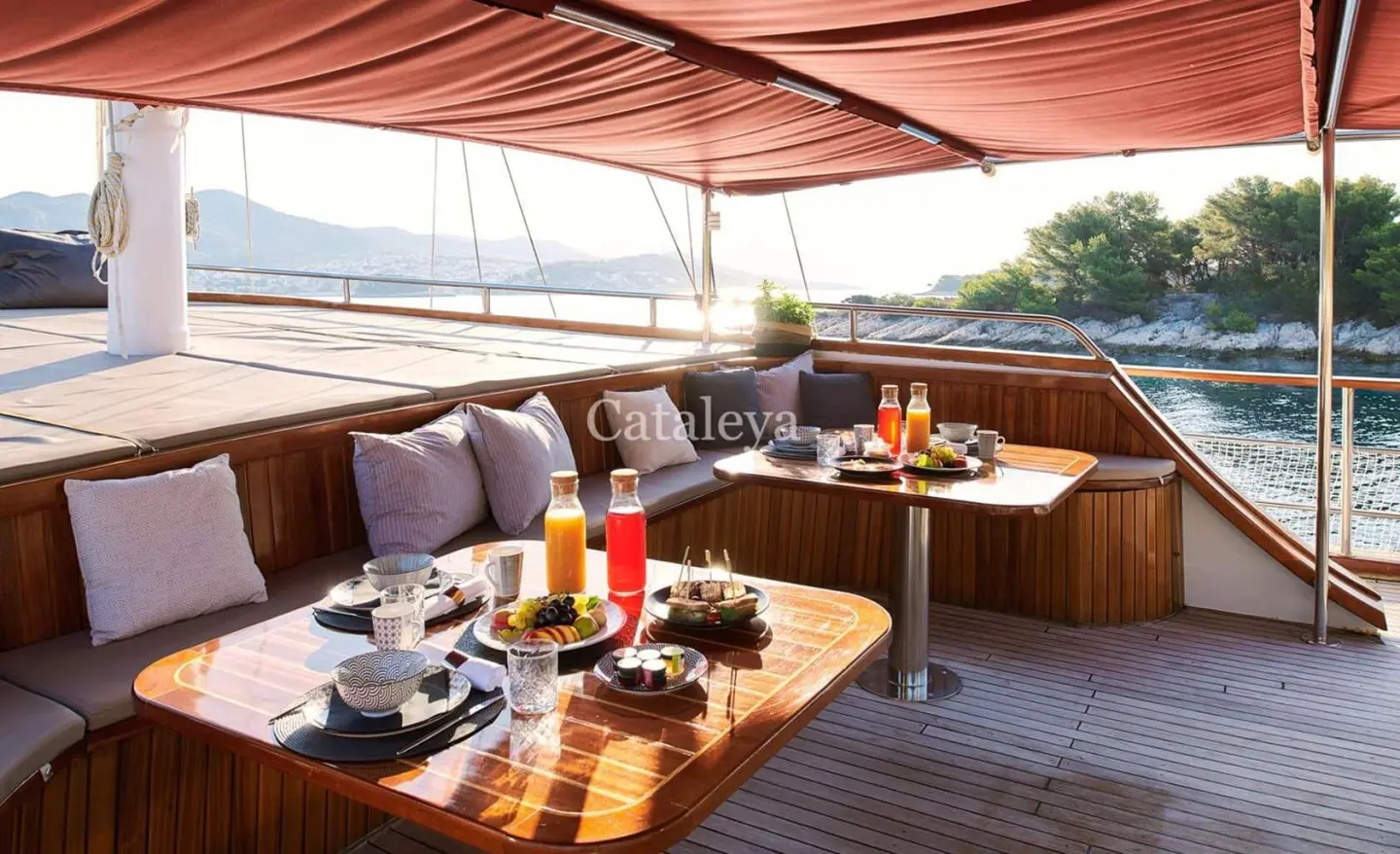 Comfortable yacht deck seating under a red awning with a table set for dining
