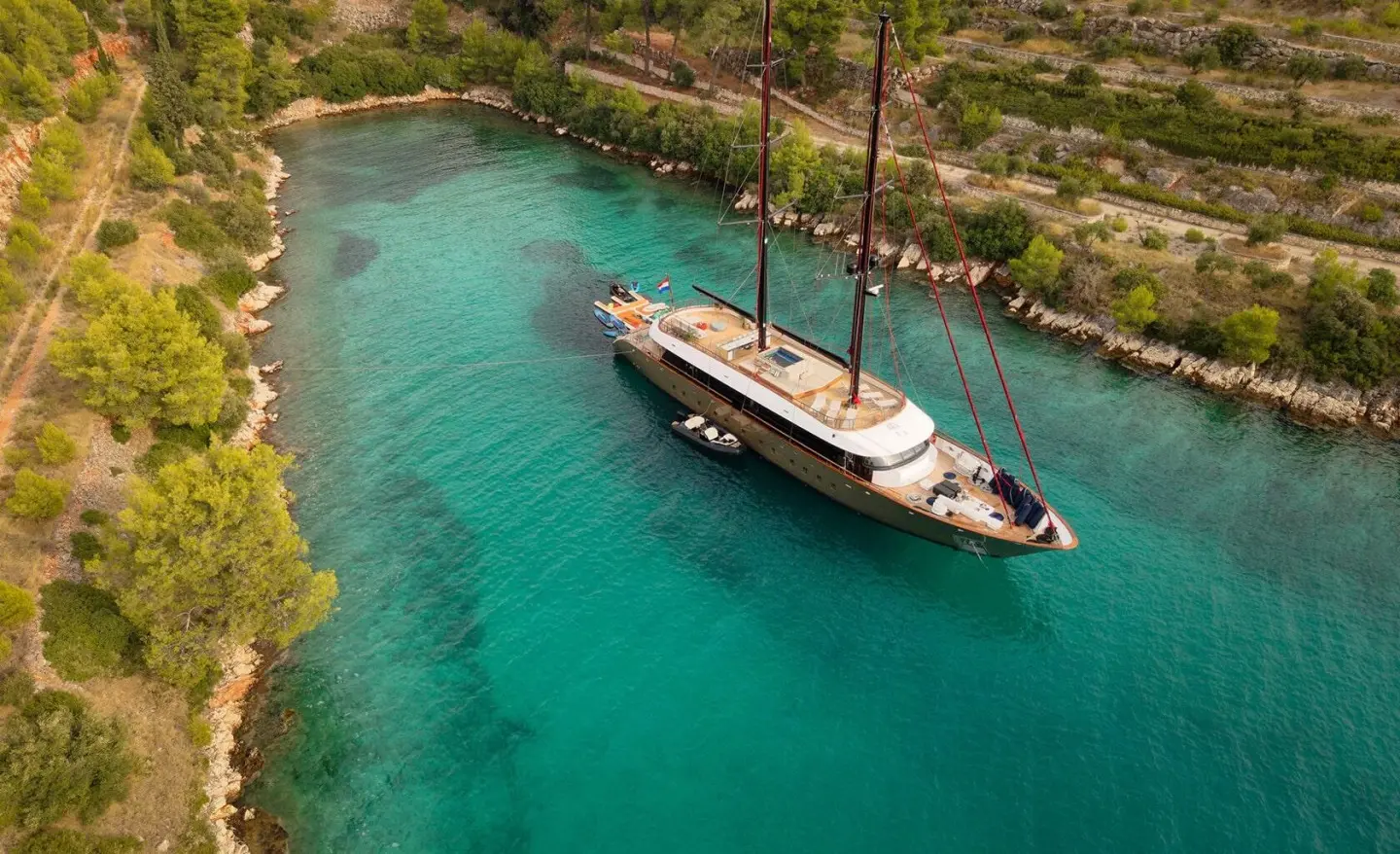 Anetta yacht anchored in turquoise coastal inlet with trees and rocky shore