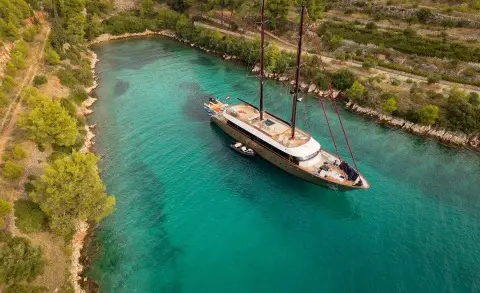 Anetta yacht anchored in turquoise coastal inlet with trees and rocky shore