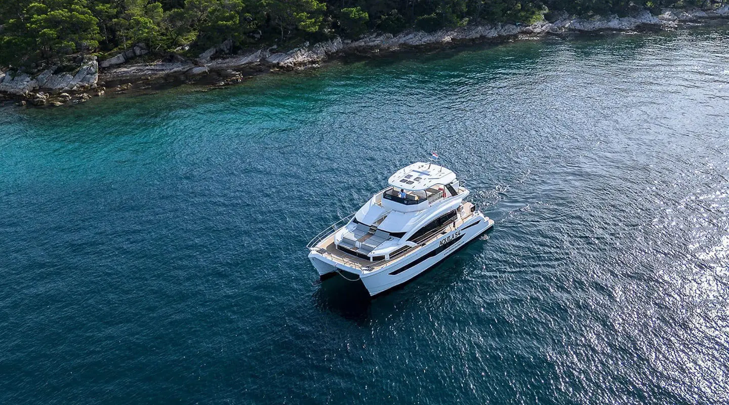 By My Side yacht cruising emerald blue waters near rocky coastline