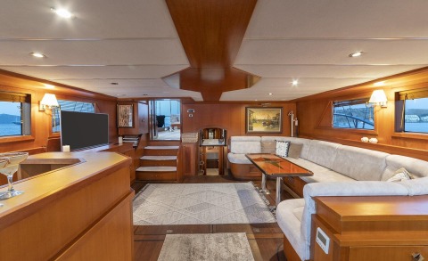 Arabella yacht interior with wooden cabinets, a curved sofa, central coffee table, and a TV screen in a luxurious saloon