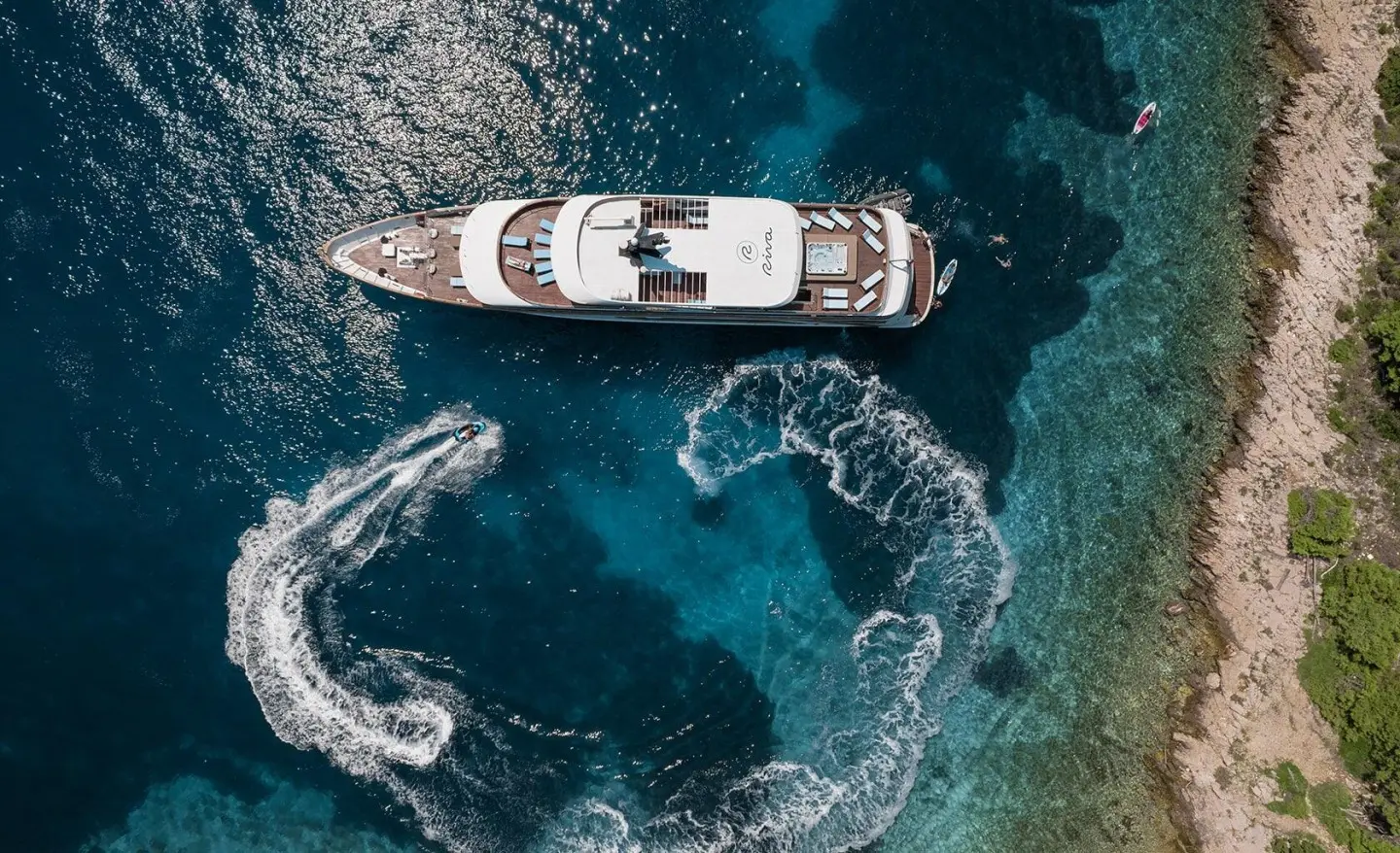 Aerial view of a sleek Riva luxury yacht anchored near rocky coastline