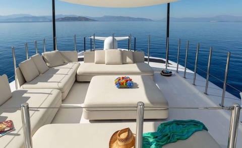 White cushioned L-shaped seating on the Sea Wolf yacht at the bow, flower arrangement on a table, blue sea and distant horizon