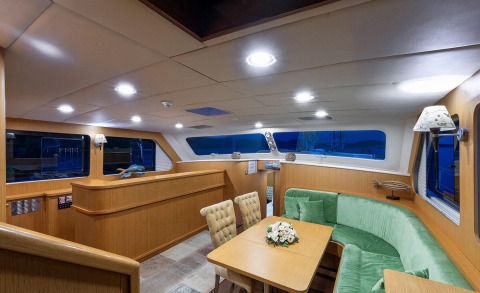 Wooden interior of Artemis yacht with a table and seating; windows showing night view outside