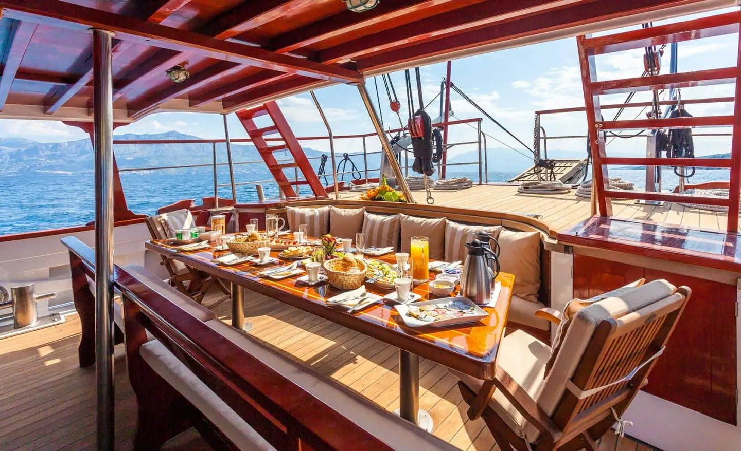View along a sunlit yacht dining deck with table settings and chairs