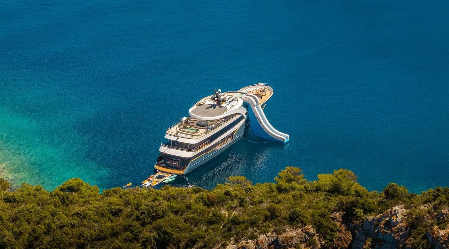 Yacht Bella anchored near rocky coastline at sunset with clear blue water