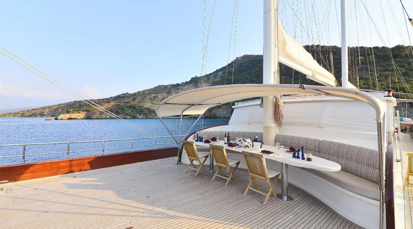 Open deck with table and chairs set for dining, sea and coastline in background