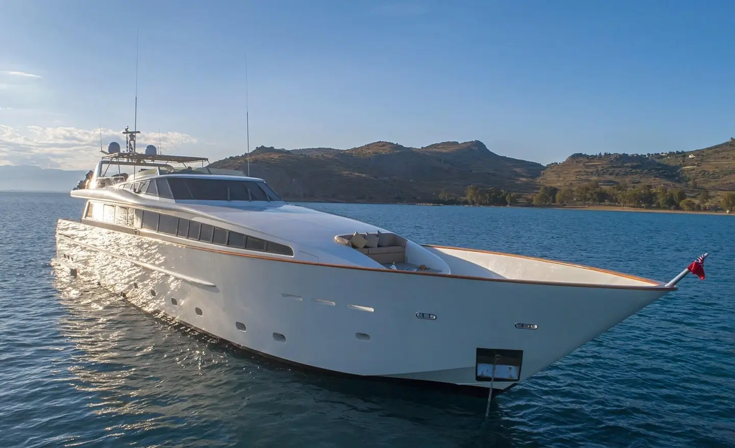 Aquila luxury yacht anchored offshore at sunset with calm blue water