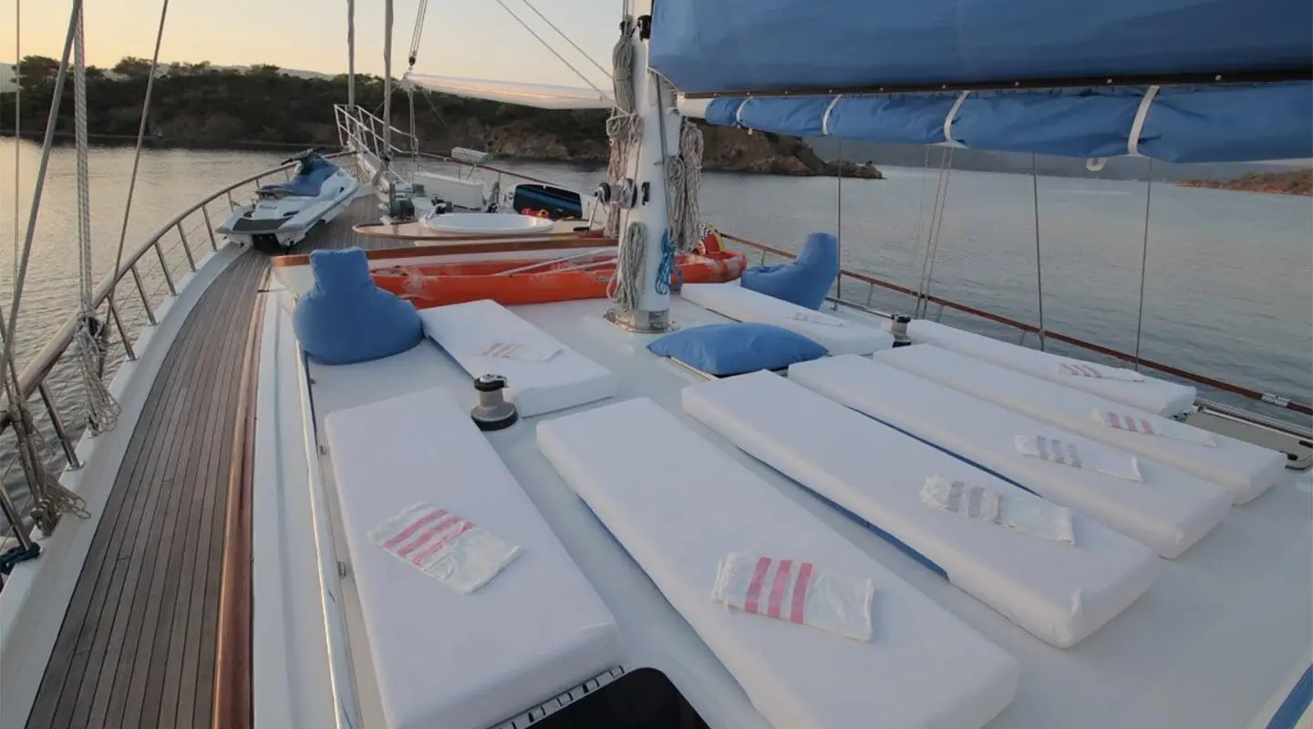 Sun deck aboard a gulet with white cushions and blue pillows at sunset