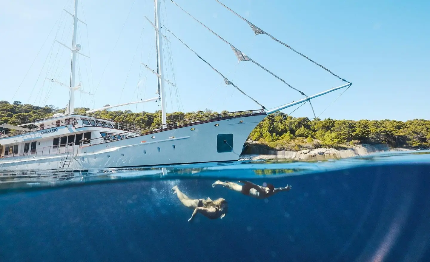 Corsario yacht anchored beside calm blue water under clear sky at sunset