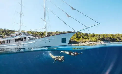 Corsario yacht anchored beside calm blue water under clear sky at sunset