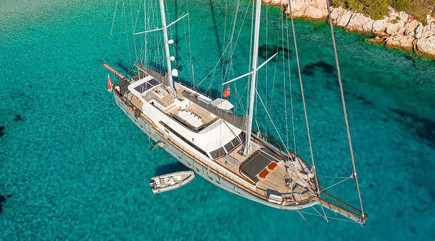 Yacht Virtuoso anchored in turquoise water at sunset, gulet-style sails down