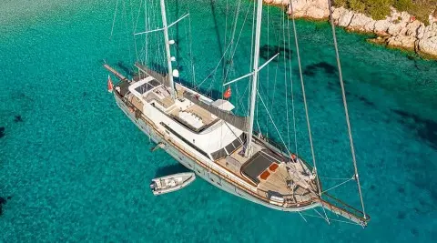 Yacht Virtuoso anchored in turquoise water at sunset, gulet-style sails down