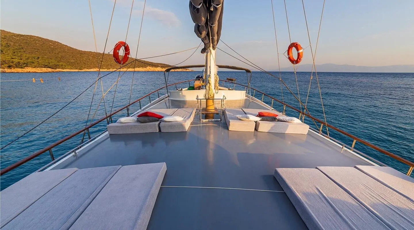 Sunlit gulet deck with cushions facing forward and the sea