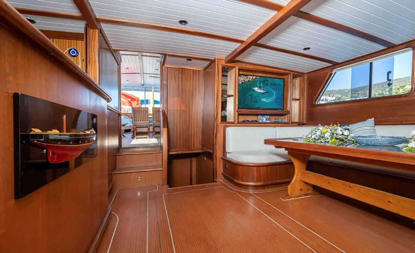 Inside Bodrum Queen yacht: wooden deck, dining table, chairs, and porthole view