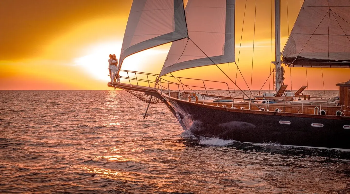 Sailing yacht Smart Spirit cutting through sunset waters with orange sky and sails
