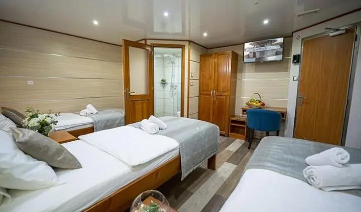 Yacht Karizma cabin interior with three beds, wood paneling, and bedside lamps