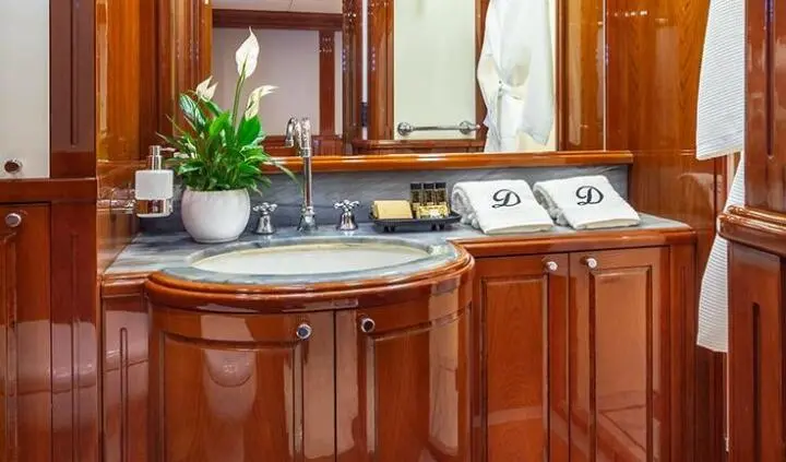 Divine yacht cabin; marble countertop sink with polished wood cabinetry and a potted plant
