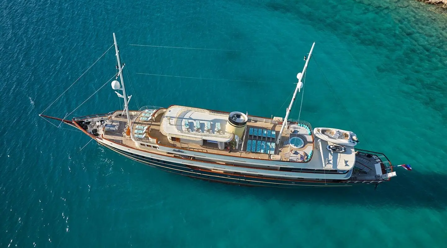 Yacht Casablanca anchored in turquoise sea, wooden deck, white hull, sails stowed