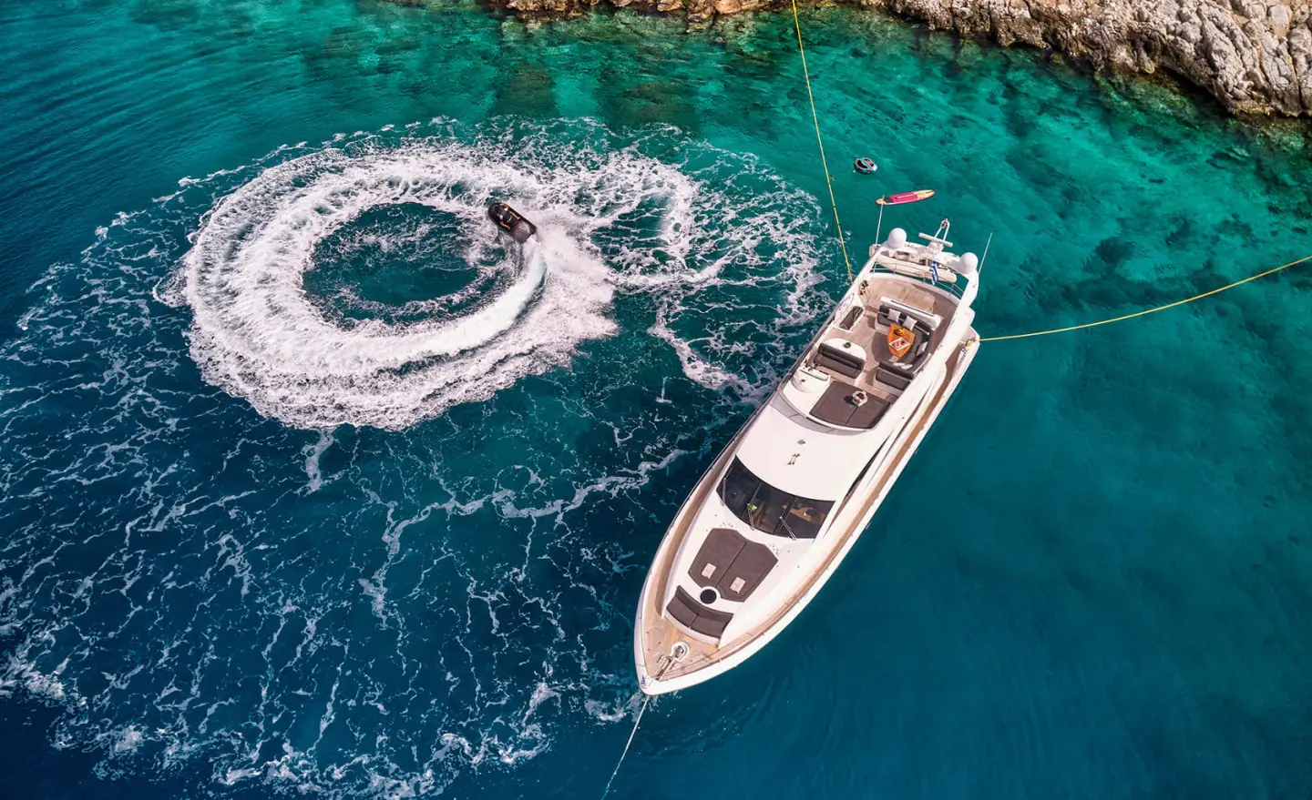 A white luxury motor yacht named M Five sails near turquoise water with a small boat nearby