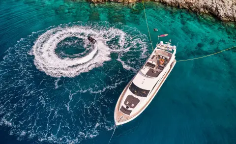 A white luxury motor yacht named M Five sails near turquoise water with a small boat nearby