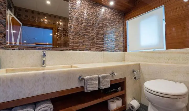 Yacht cabin with brick wall, large window, beige bed, wooden accents, ensuite bath