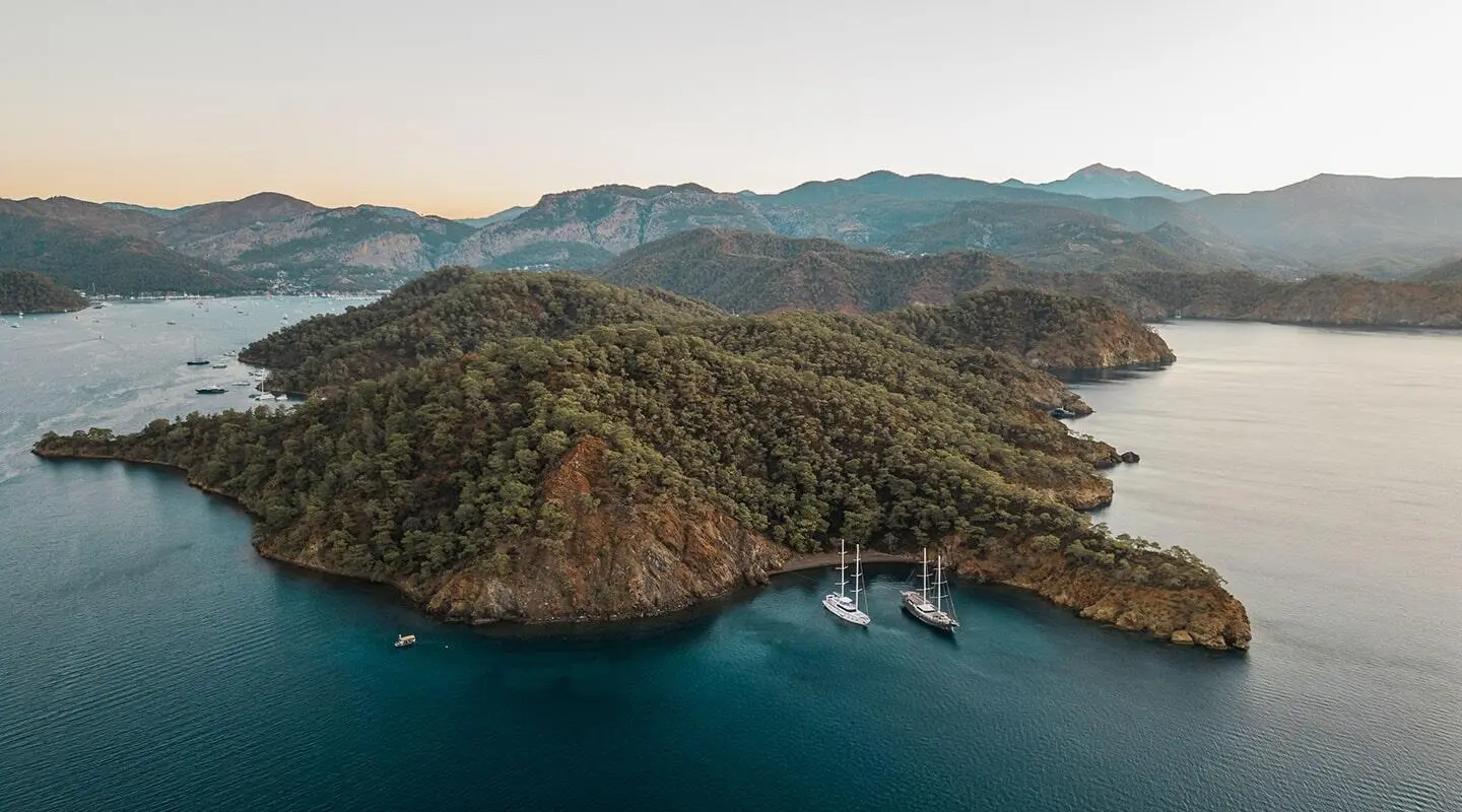 Aerial view of a luxury gulet anchored near rocky islands at sunset