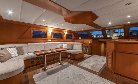 Arabella gulet interior with wood paneling, grey cushioned sofa, wooden table, and night view through windows