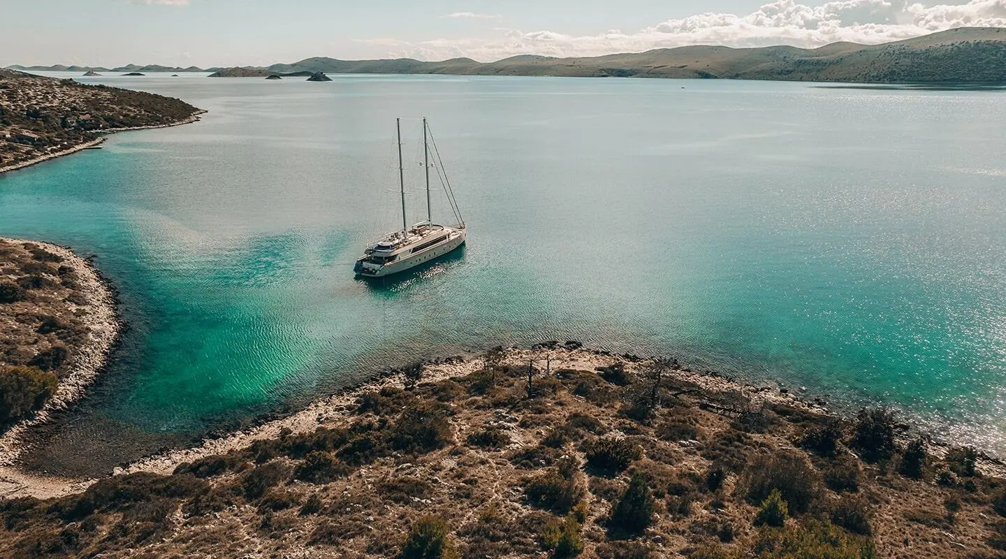 Maxita yacht anchored near turquoise shoreline with clear sea and rugged coast