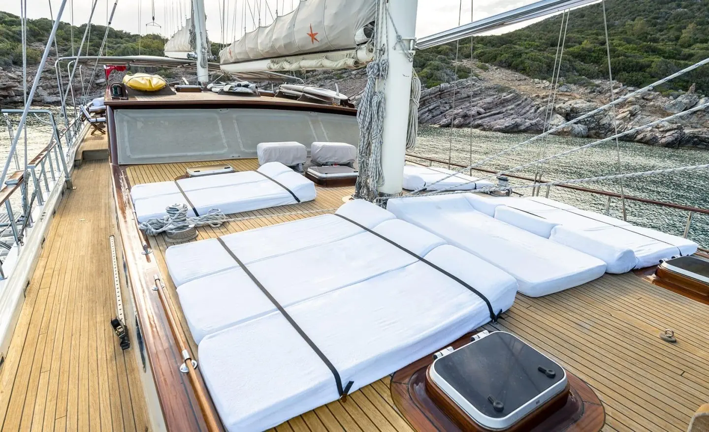 Estrella De Mar yacht deck with cushioned loungers and a sail in view at sunset