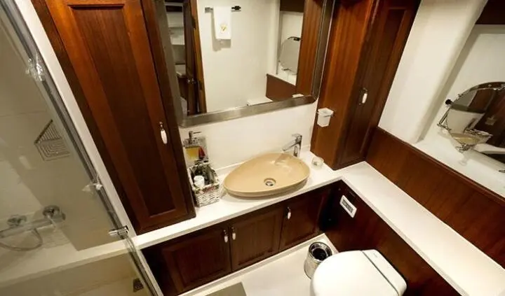 Small ensuite bathroom aboard Virtuoso yacht with sink, mirror, and wooden cabinetry