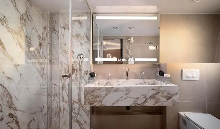 Elegant yacht cabin bathroom with marble countertop, sink, mirror, and frosted glass shower