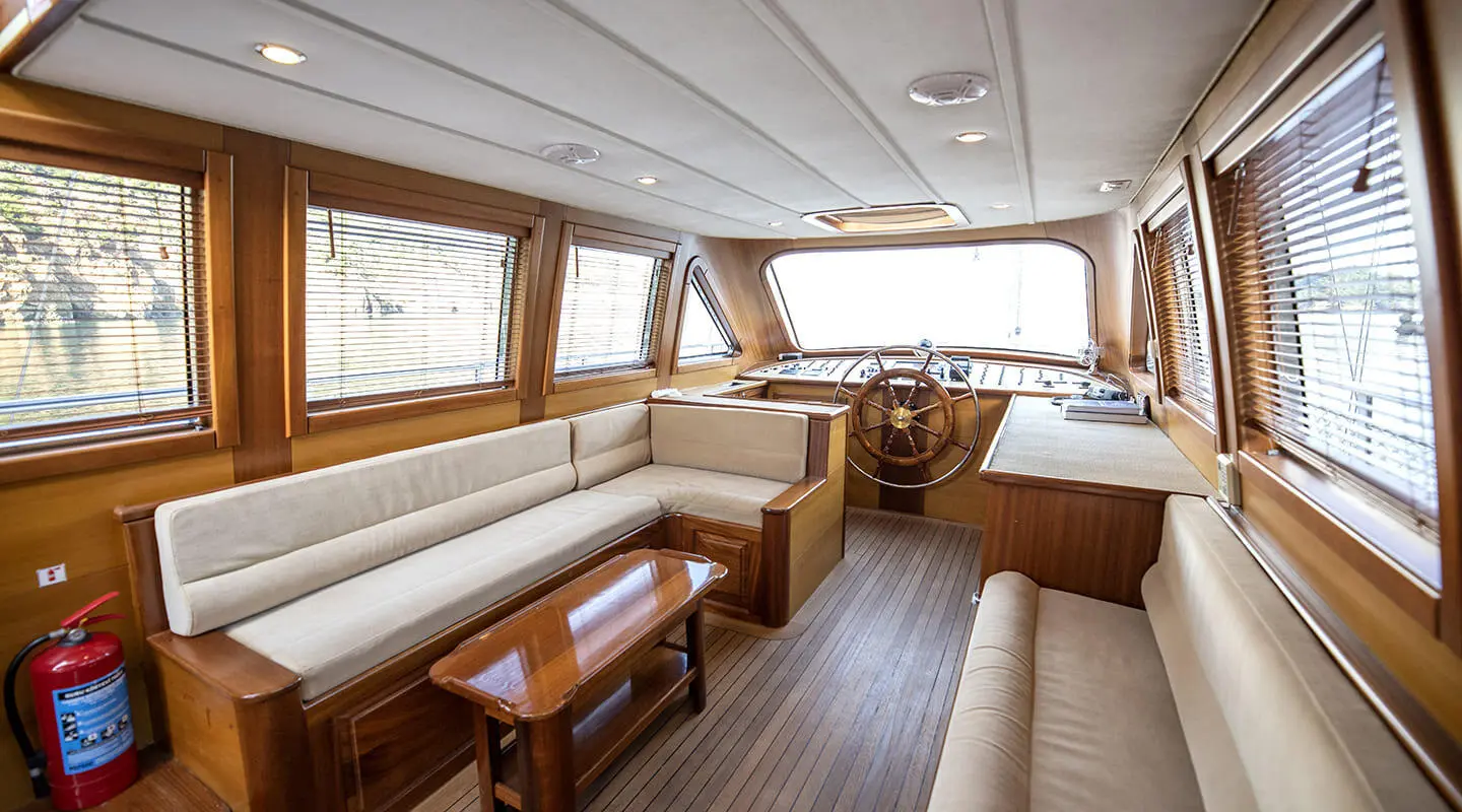 Luxurious yacht interior with seating area, wooden tables, and ample windows