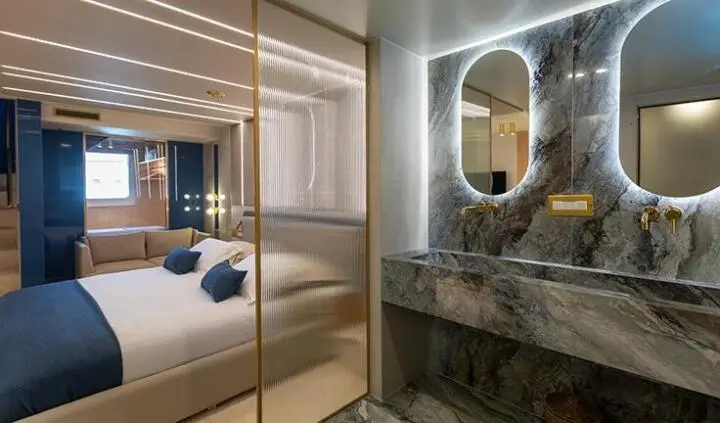 View of a yacht master cabin with king bed, ensuite bathroom, circular mirror