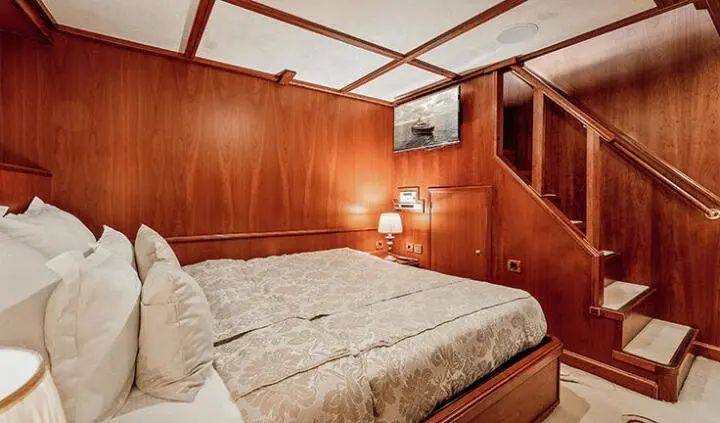 Seagull II cabin interior with plush bed, wood-paneled walls, and staircase to upper deck