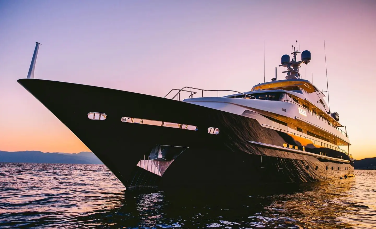 Xana luxury yacht at sunset, sleek dark hull, reflective water, golden sky