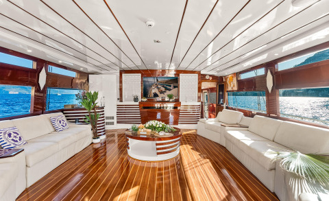 luxury yacht interior on wooden deck with beige sofas and central table, bar area with TV in back
