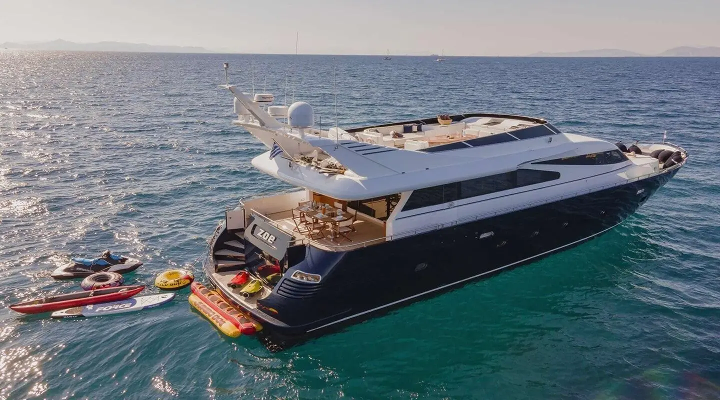 A sleek luxury yacht named Zoi anchored in clear blue water with sunlit decks