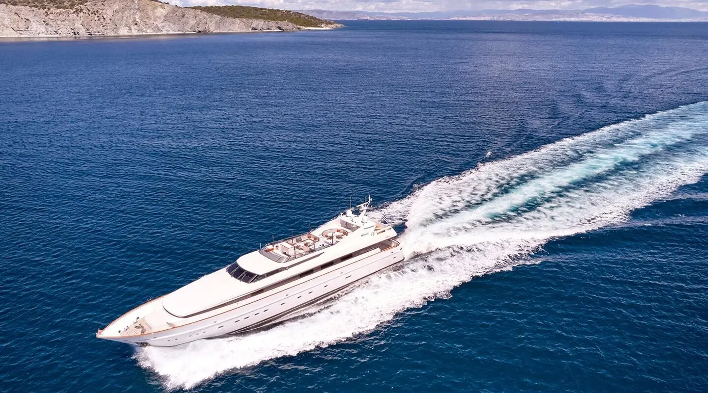 Mobius yacht cutting through blue sea, white wake trailing behind, sails and deck visible