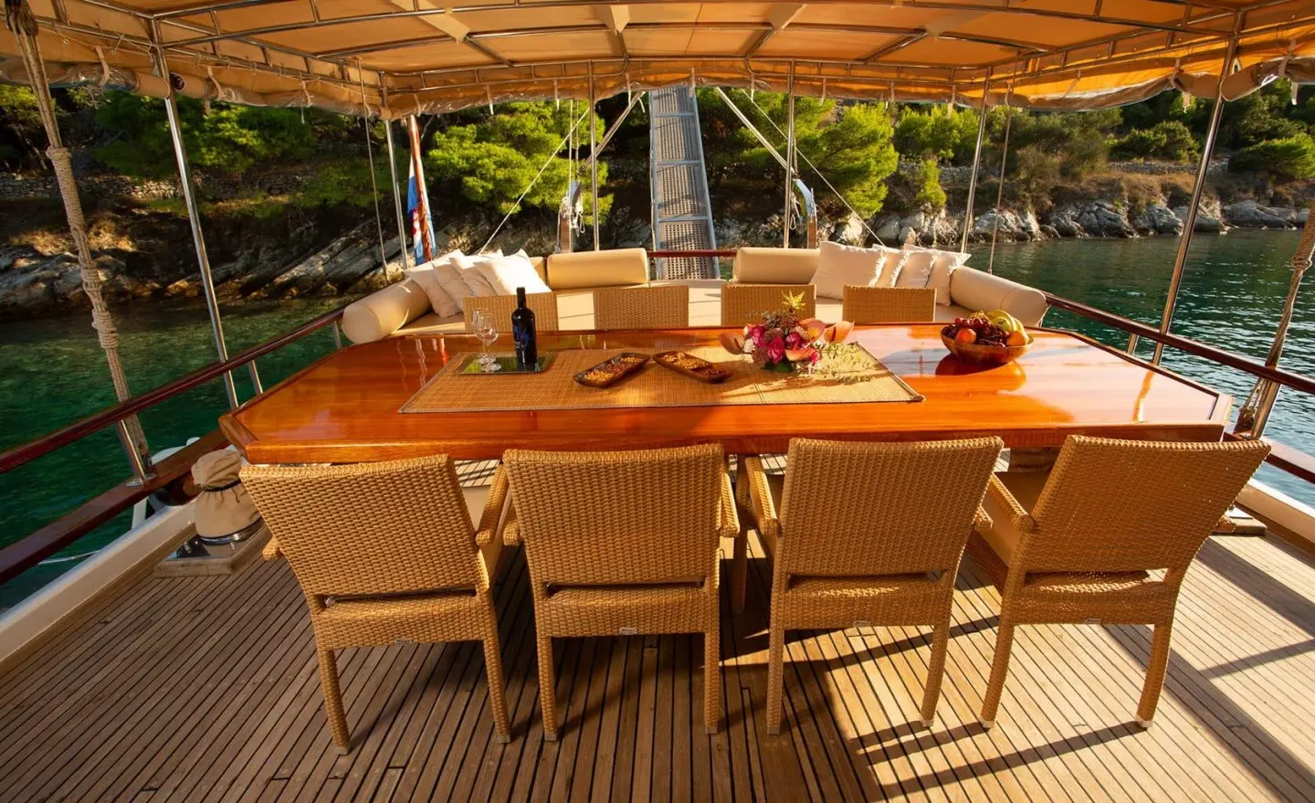 Malena yacht dining area aboard: wooden table set with chairs under shaded deck