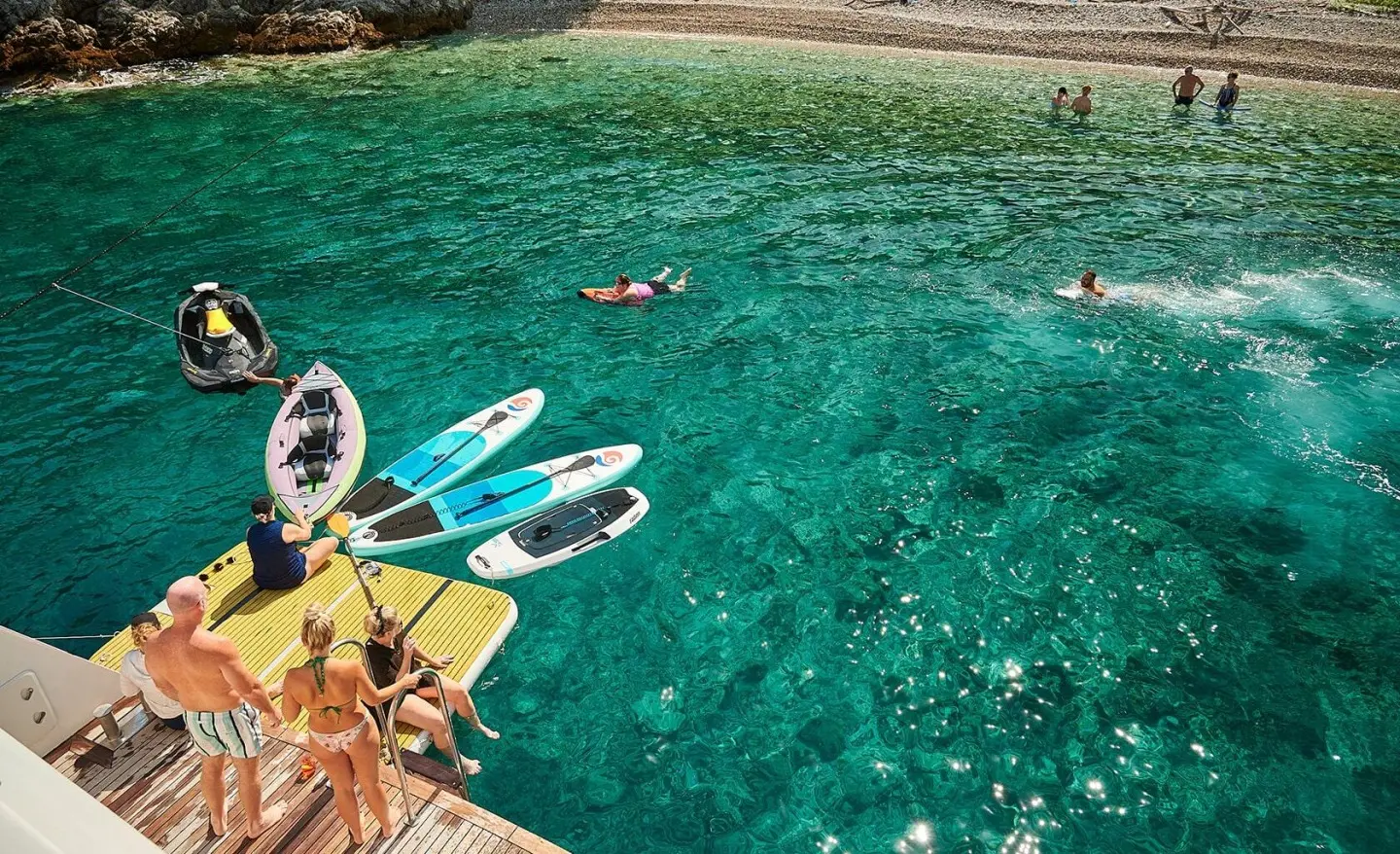 Overhead view of a blue-green sea with a yellow inflatable raft and two kitesurf boards near a coastline