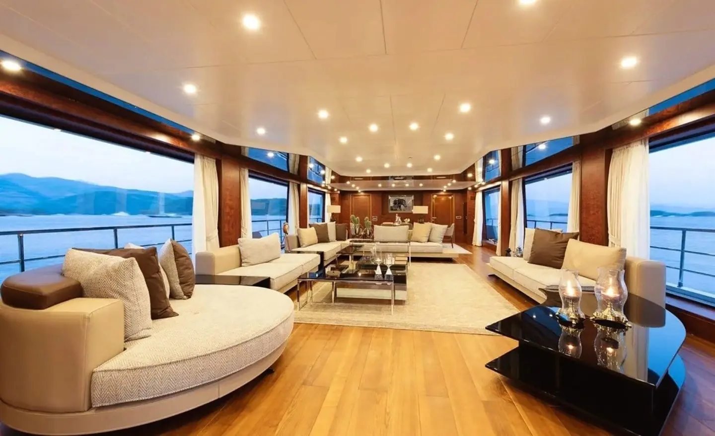 Luxurious yacht interior on Ocean Breeze with seating, wooden deck, and ceiling lights at sunset