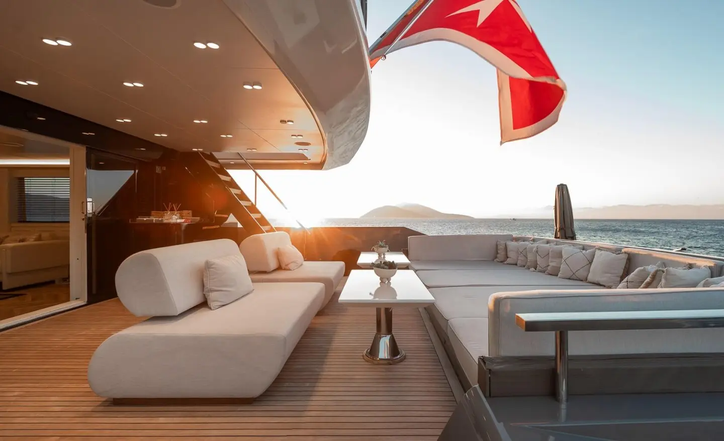 Sunlit yacht Illusion II deck with seating and a red sail in the background