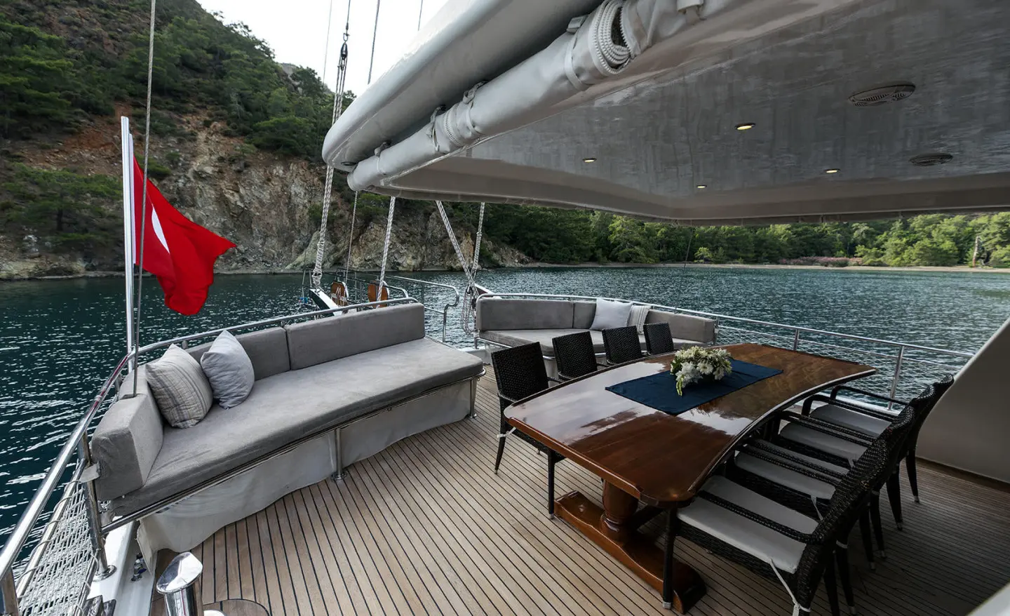 Kayhan 3 yacht deck dining area with seating, table, and sun loungers on teak deck