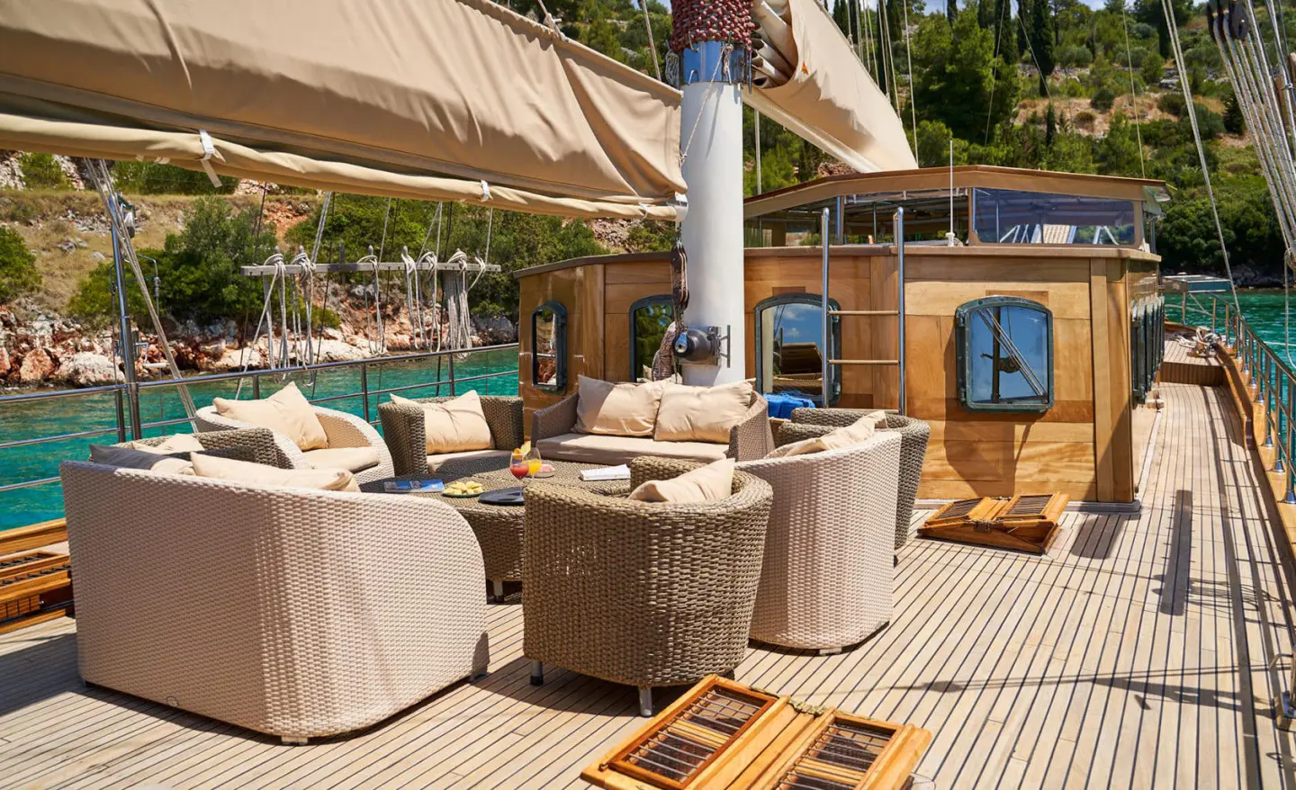 Lounge area with cushioned seating on a wooden yacht deck, cabin and rigging