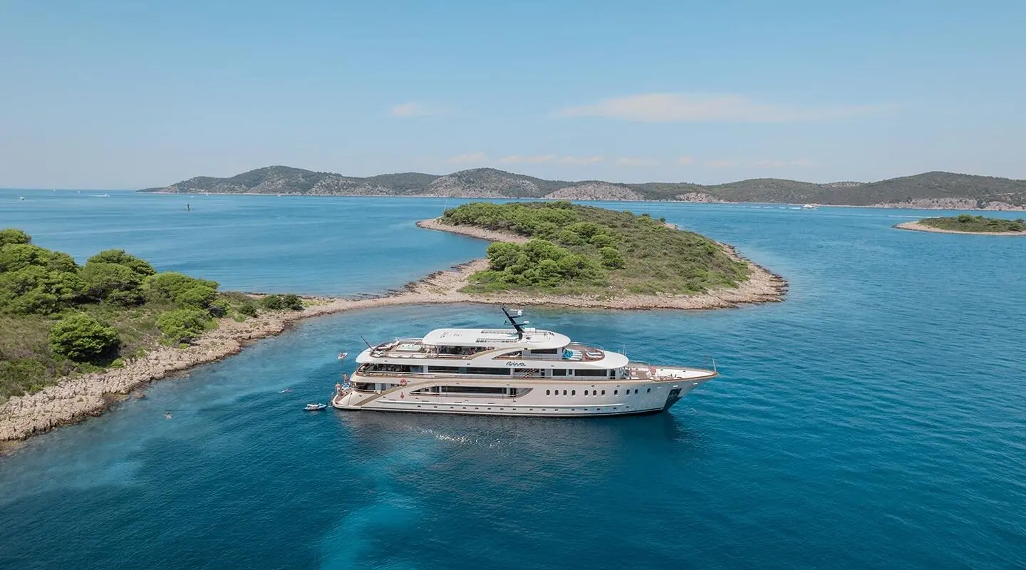 White yacht anchored in calm blue sea near small green islets