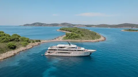 White yacht anchored in calm blue sea near small green islets