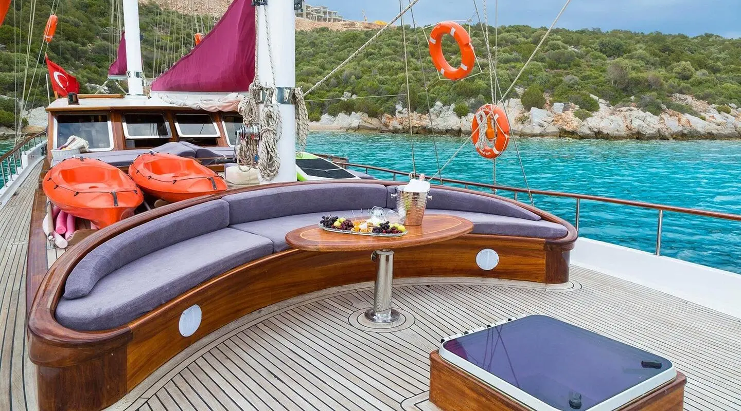 Primadonna yacht deck with polished wood, blue sea, and sailing rig at sunset