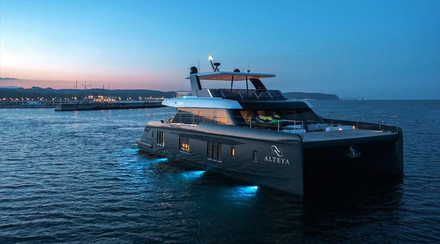 Alteya luxury yacht anchored at dusk with dark hull, blue water, and sunset glow